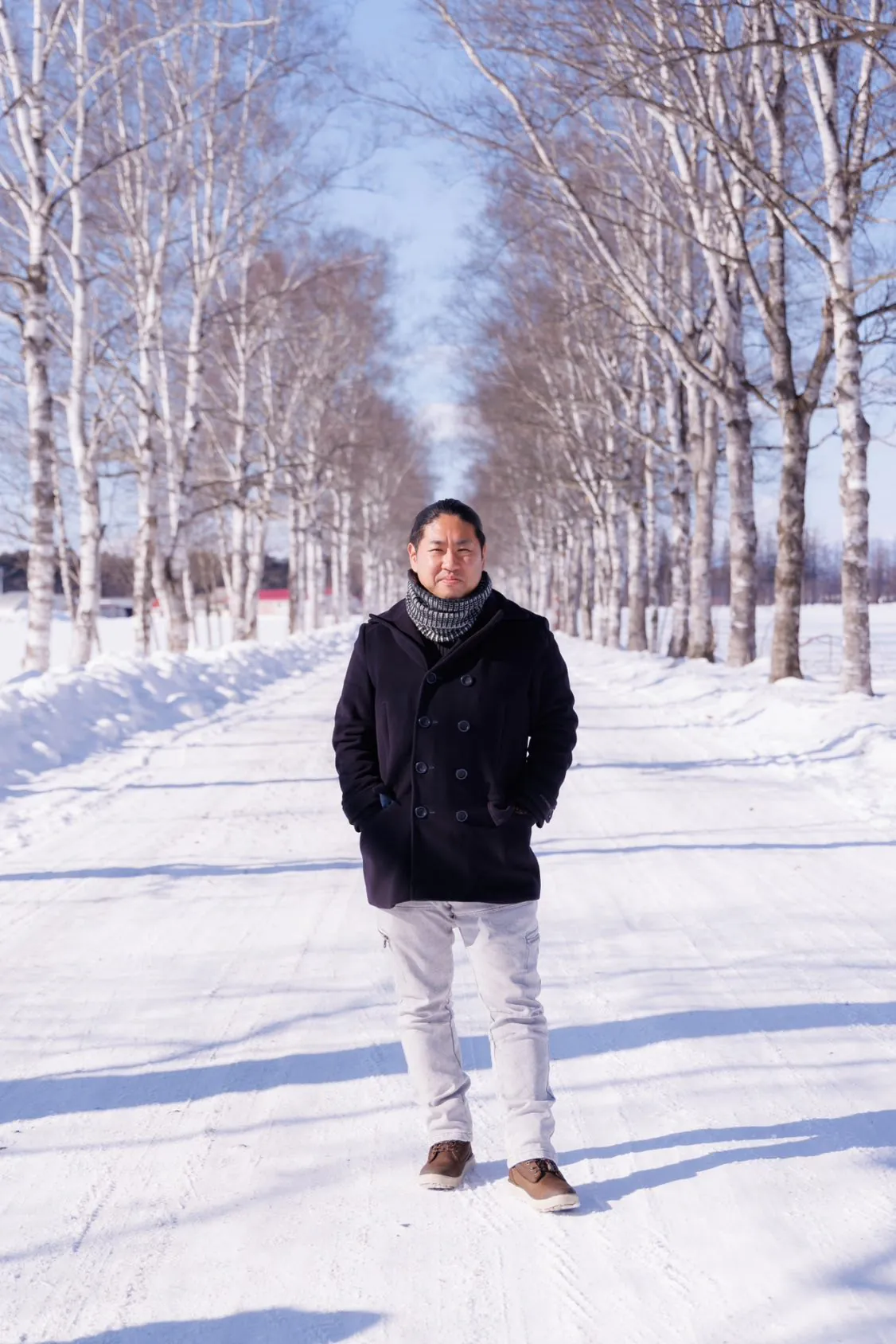 雪の白樺並木に立つ木村善幸
